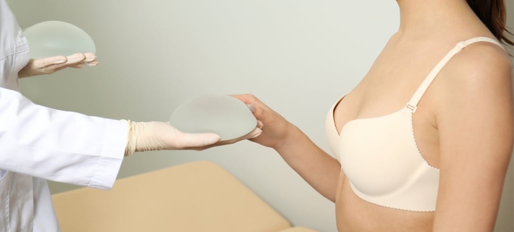Doctor comparing two breast implant sizes with a patient, illustrating the trend toward smaller, more natural implant sizes