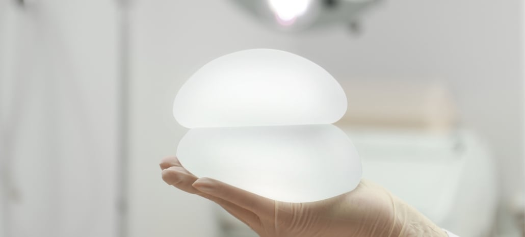 Silicone breast implant held in the operating room, related to en bloc capsulectomy and implant removal surgery