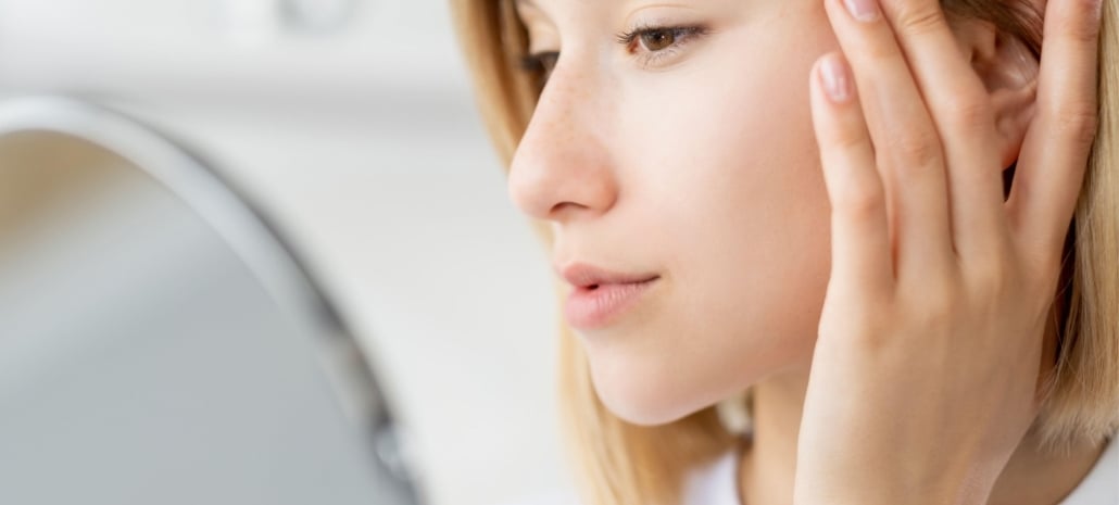 Woman closely examining her face in a mirror, reflecting the importance of understanding facelift risks before surgery