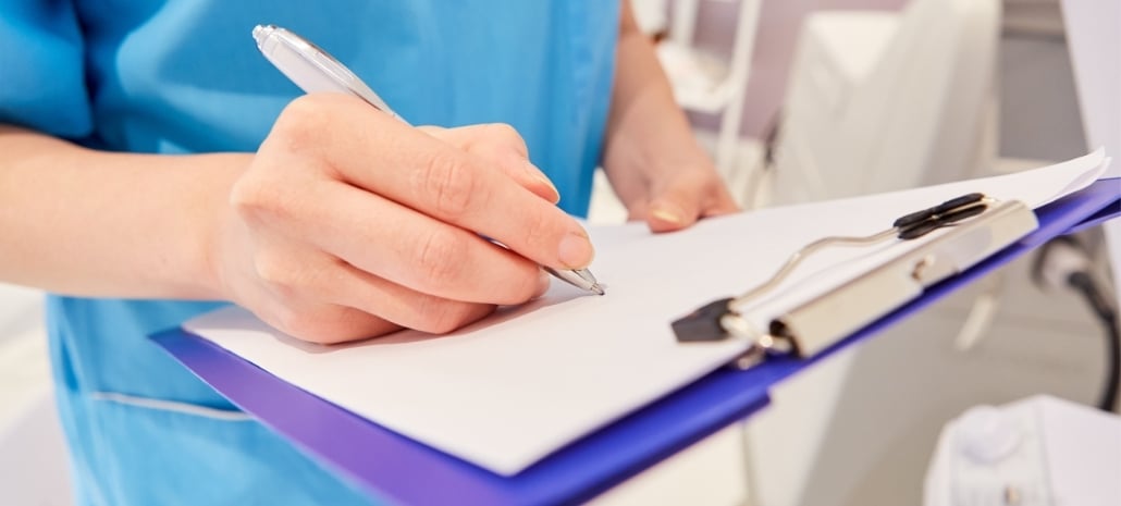 Medical professional writing notes on a clipboard, representing a risk management checklist for breast augmentation