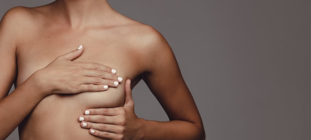 Woman gently touching her breast, representing the natural tissue capsule that forms around breast implants