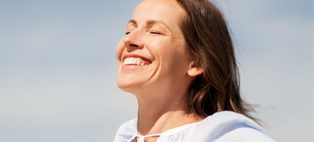 Joyful mature woman smiling in natural sunlight, representing confidence addressed in the facelift open letter