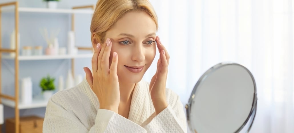 Woman examining her face in a mirror, reflecting on natural facelift results
