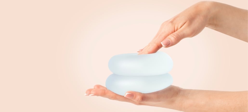 Close-up of hands holding a saline breast implant, illustrating the pros and cons of implant types